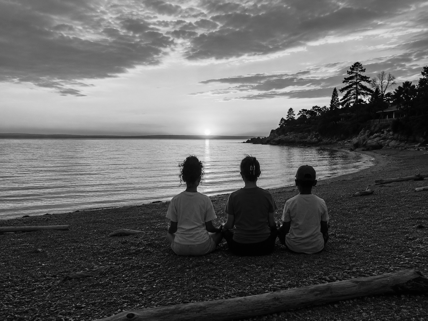 Three children sitting on a shoreline at sunset